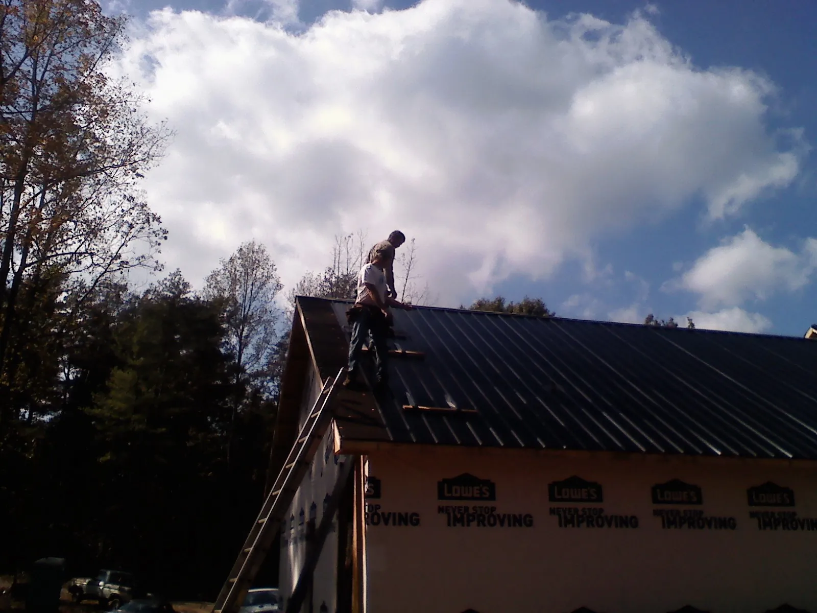 Roofer fastening dark metal panels high against a cloudy sky, from a Roof Inspection job in Albany